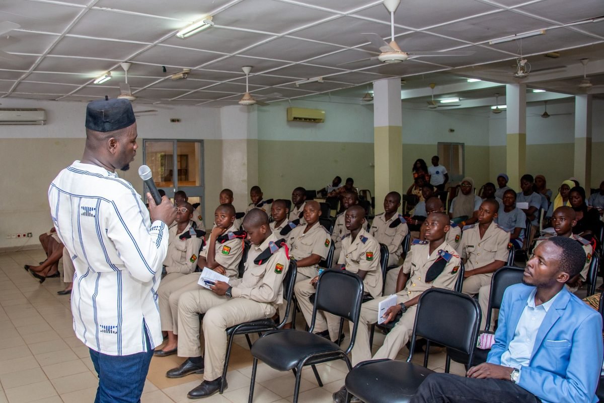 An instructor with a microphone addressing uniformed trainees in a training room