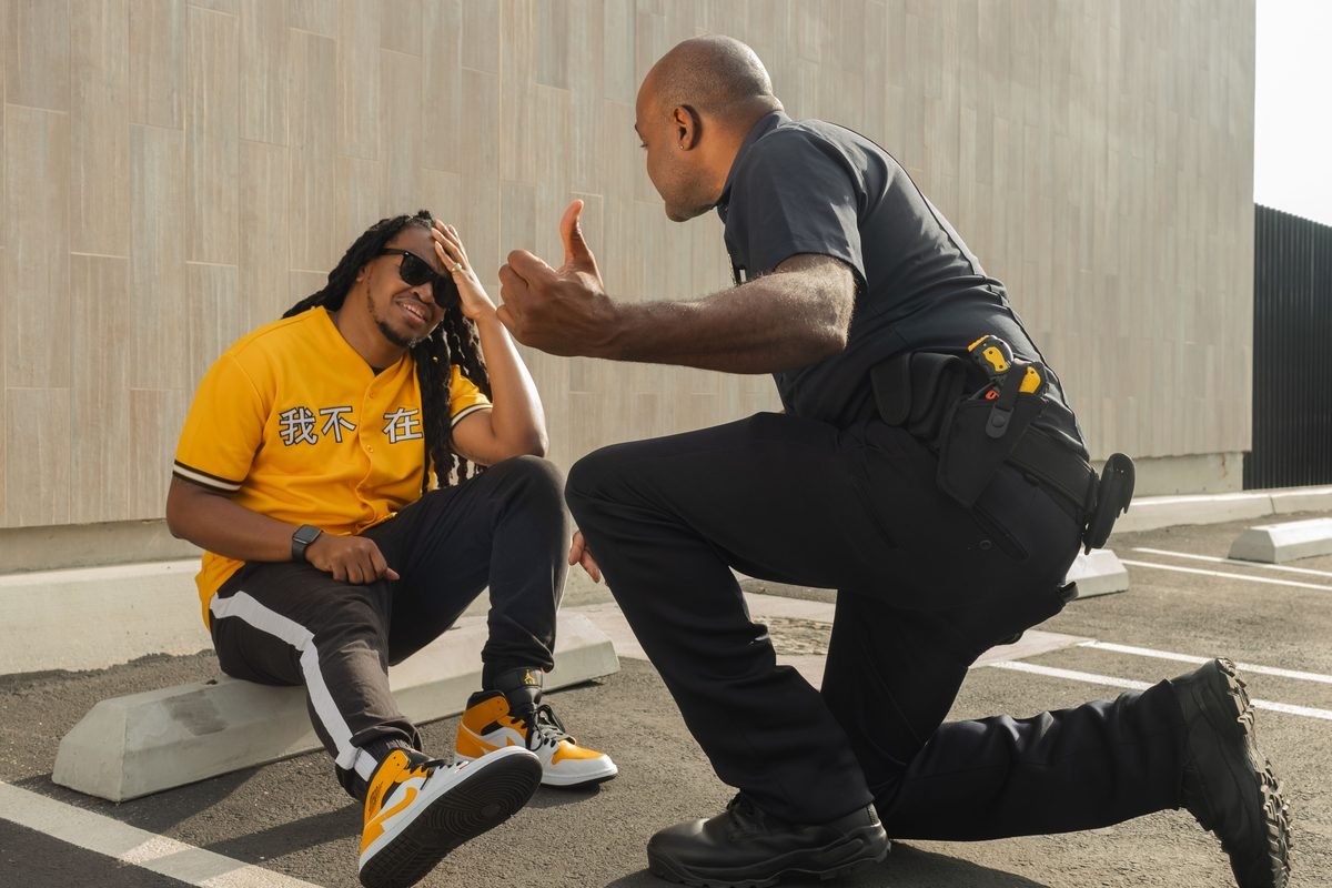 A police officer kneeling beside a seated man who is holding his head