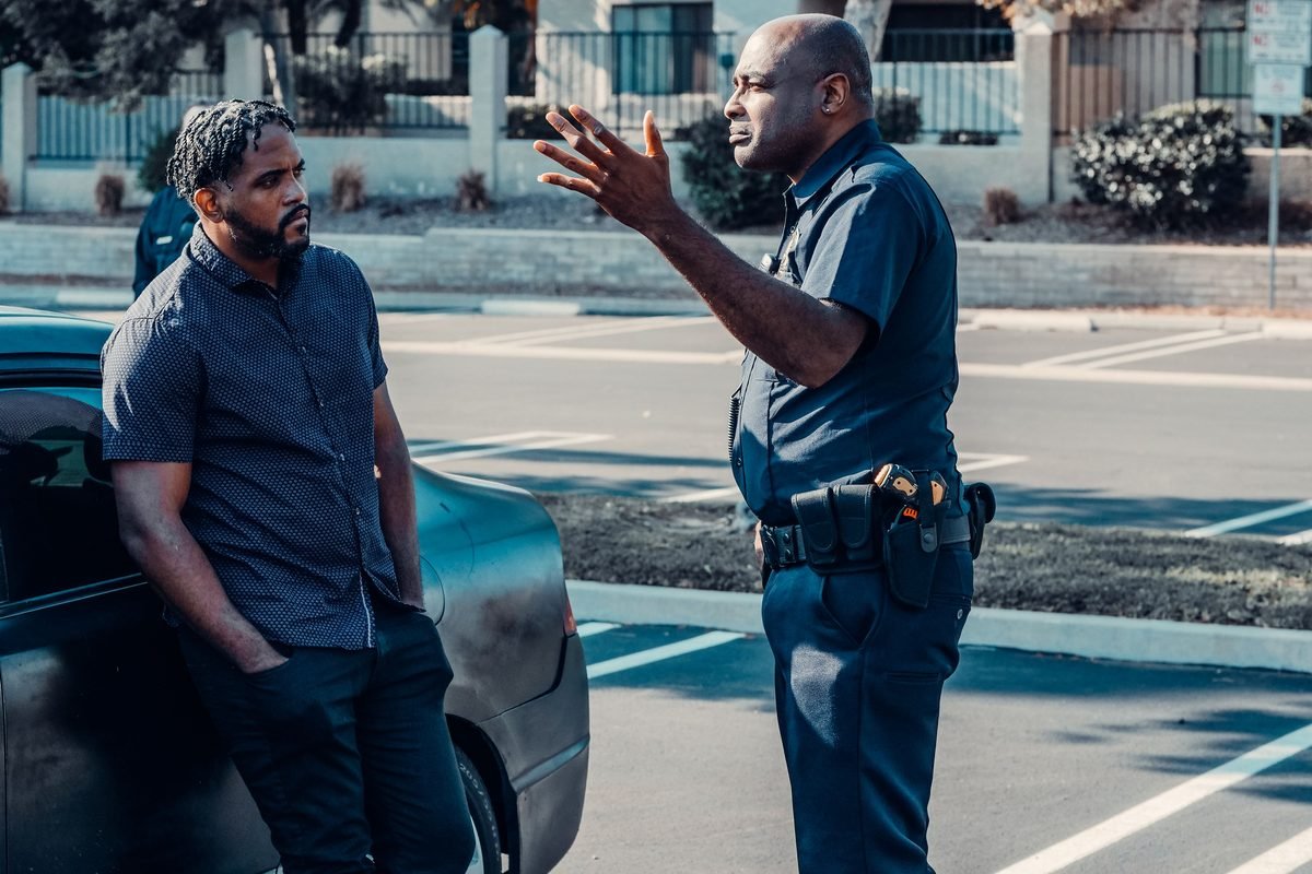 A police officer talking calmly with a man beside a car, explaining with open hands